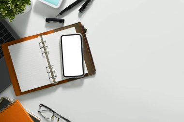 Beyaz masada boş ekran, defter, gözlük ve dizüstü bilgisayarı olan üst görünüm akıllı telefonu.