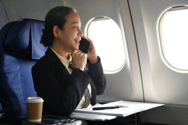 Başarılı üst düzey iş kadını yolcu pencerelerin yanındaki uçak kulübesinde otururken cep telefonuyla konuşuyor..