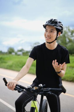 Parkta bisiklet sürerken, kulaklıkla konuşan mutlu Asyalı bisikletçi..