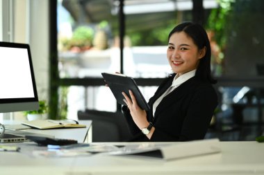 Resmi kıyafet giymiş çekici bir iş kadınının resmi. İstatistik belgelerle çalışıyor ve ofis masasında dijital tablet kullanıyor..