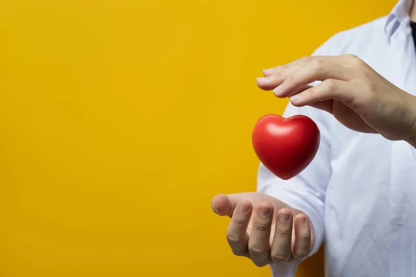 医生手牵着红心的黄色背景心脏科 捐赠和医疗理念 — 图库照片