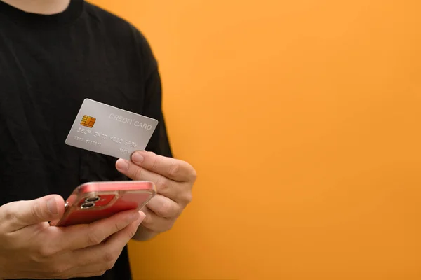 stock image Man holding a credit card and smartphone isolated on yellow background. E-commerce, banking service, shopping online.