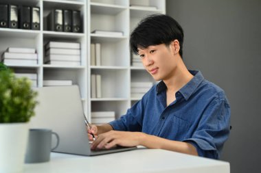 Çevrimiçi veri pazarı analizi yapan Asyalı girişimci, modern işyerinde dizüstü bilgisayar kullanıyor.