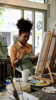 Sanat sınıfında tuvale resim yapan neşeli Afrikalı Amerikalı kadının dikey çekimi. Sanat, yaratıcı öğrenme ve eğitim kavramı.