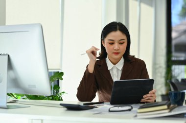 Modern ofiste oturmuş dijital tablet hakkında internet bilgilerini analiz eden şık genç iş kadını..