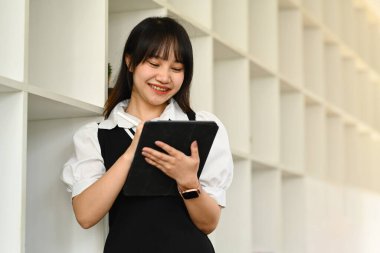 Dijital tablet kullanan, çalışan, iletişim kuran, kütüphanede internette sörf yapan gülümseyen kadın portresi.