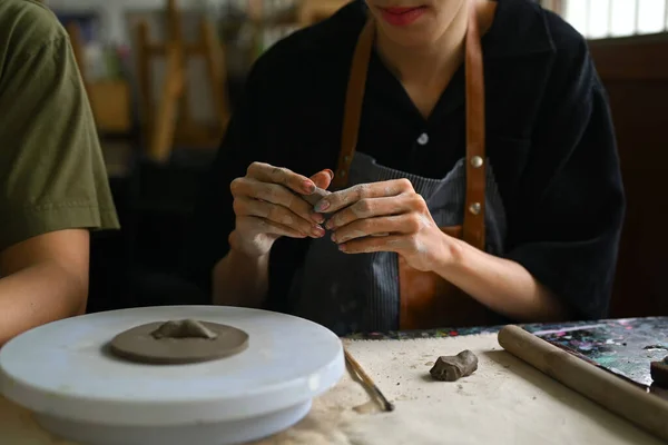 stock image Craftspeople wearing aprons working with raw clay, shaping and decorating pottery in workshop.