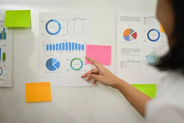 stock image Female economist analyzing sales statistics document, discussing information on whiteboard with her colleague.