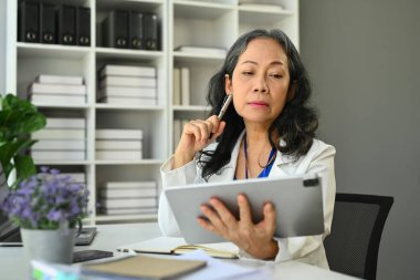 Beautiful elderly business woman analyzing financial data, stock market information on digital tablet.