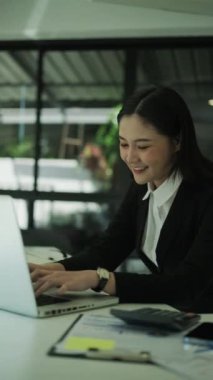 Profesyonel kadın muhasebecinin dizüstü bilgisayara bakıp klavyede daktilo kullandığı dikey çekim..