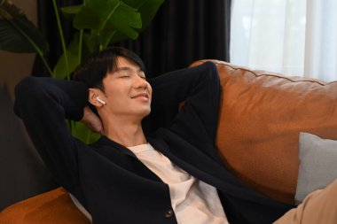 Mutlu Asyalı adam rahat kanepeye uzanmış stressiz ve huzurlu bir evde keyfine bakıyor..