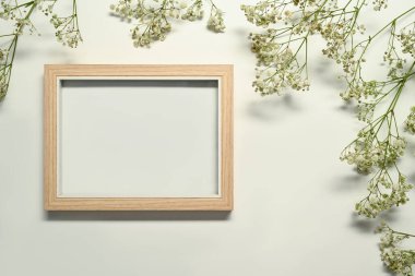 Beyaz bebekli boş ahşap çerçeve beyaz arka planda soluk çiçekleri.