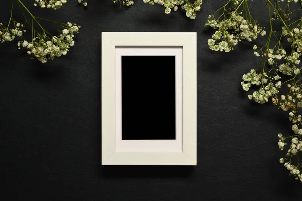 Empty wooden picture frame with white babys breath flowers on dark background.