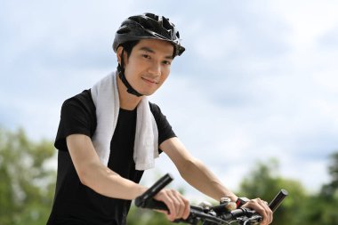 Spor kıyafetleri içinde Asyalı bisikletçi ve halka açık bir parkta kask bisikletçisi. Spor, açık hava aktiviteleri ve sağlıklı yaşam tarzları..