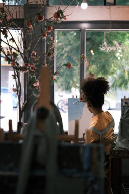 Bir kadın ressamın sehpanın önünde oturup sanat stüdyosundaki tuvalde sanat eserleri yaratması..