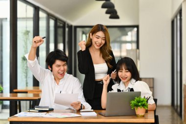 Mutlu iş adamları dizüstü bilgisayara bakıyor ve evet jestleri yapıyor, proje başarılarını kutluyorlar..