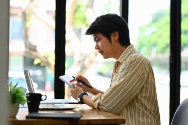Bilgisayarı kullanan genç işadamının yan görünüşü, masadaki istatistiksel belgelerle çalışıyor.