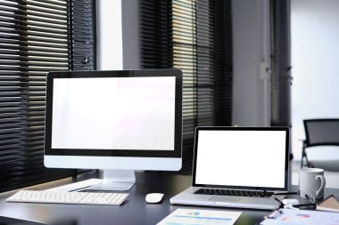 Boş bilgisayar monitörü, dizüstü bilgisayar, belge ve malzemelerle modern ofis içi.