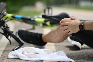 Dışarıda bisikletin yanında oturan yaralı dizli bir adam bisikletten düşüyor. Bisikletten kaynaklanan kavram kazası.