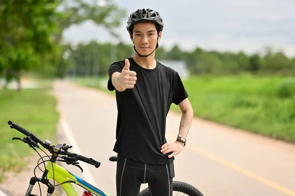 Smiling man cyclist in sport clothes and helmet showing thumb up sign. People, sport, emotions and healthy lifestyle.