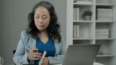 Gülümseyen orta yaşlı iş kadını dizüstü bilgisayarda web sitesi izliyor ve not defterine notlar alıyor..