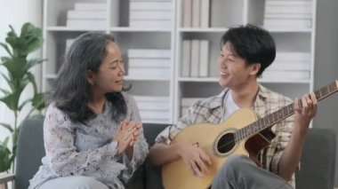 Genç Asyalı adam evde gitar çalıyor ve büyükannemle şarkı söylüyor. Mutlu aile, eğlence, eğlence aktivitesi konsepti.