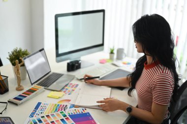 Renk paletiyle çalışan genç yaratıcı kadın grafik stüdyosunda tasarım projesi için renk örnekleri seçiyor..