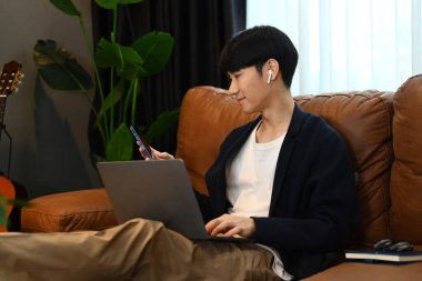 Gündelik giyinen çekici bir adam koltukta dinlenir ve akıllı telefon kullanır. İnsanlar ve teknoloji kavramı..