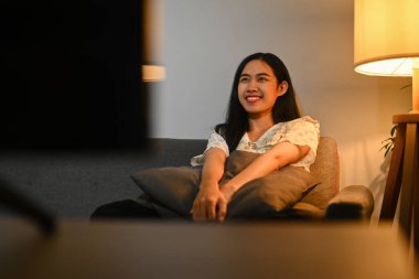 Gülümseyen Asyalı kadın akşam evde yalnız başına romantik bir film izliyor...