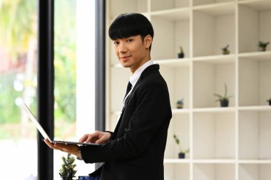 Kendine güvenen erkek yöneticinin portresi dizüstü bilgisayarla ofis masasında oturuyor ve kameraya bakıyor...