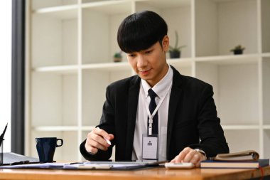 Siyah takım elbiseli Asyalı bir yönetici kağıt işi belgesi dolduruyor, ofis masasında kontrat imzalıyor...