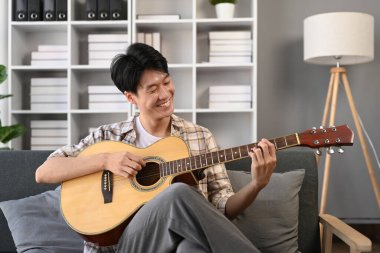 Kanepede akustik gitar çalan mutlu bir adam, rahat oturma odasında vakit geçiriyor...