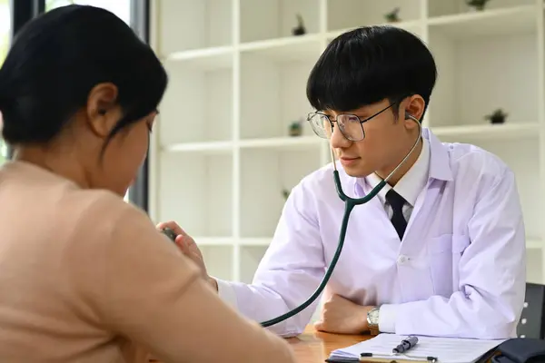 亚洲男医生使用听诊器 在检查室聆听女病人的呼吸或心跳 — 图库照片