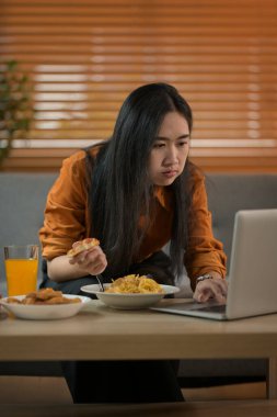 Masada spagetti ve dizüstü bilgisayar yiyen Asyalı kadın, ev konsepti ve ev hayatı üzerine çalışıyor..