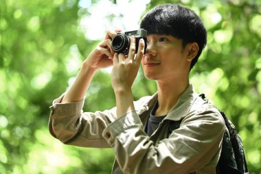 Sırt çantalı yakışıklı Asyalı erkek turist kamerayla doğa manzarası çekiyor. Seyahat, macera ve aktif yaşam konsepti..