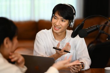 Kulaklık takan yakışıklı bir erkek radyo sunucusu. Konukla röportaj yapıyor. Ev stüdyosunda podcast yapıyor..