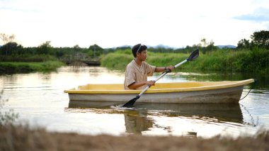 Güzel bir gün batımında gölde kürek çeken mutlu Asyalı adam. Seyahat, yalnızlık, sakinlik ve rahatlama..