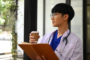 Beyaz önlüklü pratisyen hekimin görüntüsü kahve içip, başka tarafa bakıyor, gelecekteki kariyer görüşünü düşünüyor..