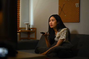 Uzaktan kumandalı güzel genç bir kadın, en sevdiği TV programının tadını çıkarıyor..