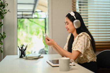 Kulaklık takan güzel genç bir kadın akıllı telefondan arkadaşlarıyla sohbet ediyor..
