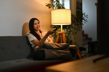 Geceleri kanepede televizyon seyreden gülümseyen genç bir kadın. Eğlence ve hobi konsepti.