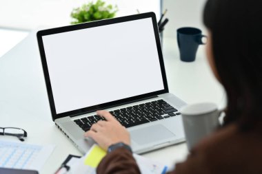 Kahve içen ve iş yerinde dizüstü bilgisayar kullanan kadın ofis çalışanının omuzlarının üstünden..