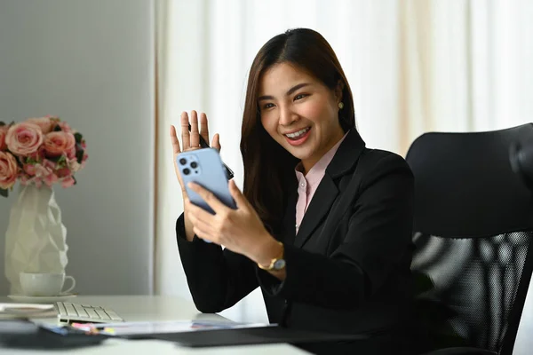 Gorgeous millennial woman waving hand, making video calling on smartphone.