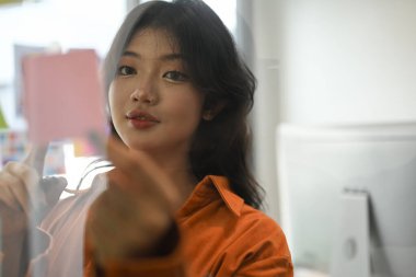 Çekici bayan yönetici şeffaf yönetim kurulu üzerinde notlar okuyor, planlama hedefleri, kurumsal işleri yönetmek.