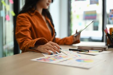 Genç tasarımcı, ahşap ofis masasındaki renk örnekleri çizelgesinden renkler seçiyor.