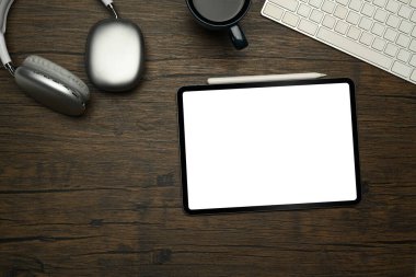 Düz konum, beyaz ekranlı dijital tablet, kahve fincanı ve ahşap masada kablosuz kulaklık..