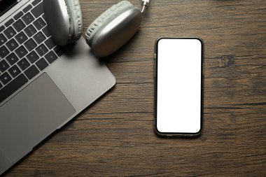 Boş ekran, kablosuz kulaklık ve ahşap masada dizüstü bilgisayarı olan üst görünüm akıllı telefon..