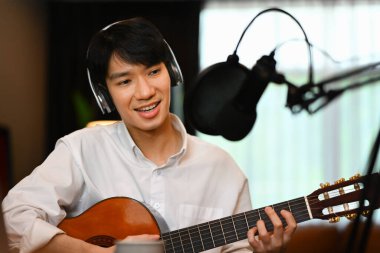 Kablosuz kulaklıklı, gitar çalan, ev stüdyosunda ses yayını yapan kendine güvenen adam.