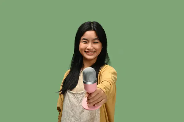 快乐的少女拿着话筒面对着被绿色背景隔离的摄像机 — 图库照片