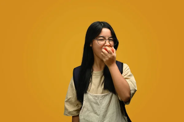 Sarı Arka Planda Elma Yiyen Neşeli Asyalı Genç Kız — Stok fotoğraf